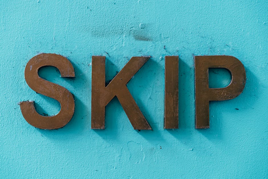 A close-up view of three uppercase brown metal letters spelling 'SKIP' affixed to a textured, bright turquoise wall. The letters have a matte finish with slight wear visible on the edges, indicating s